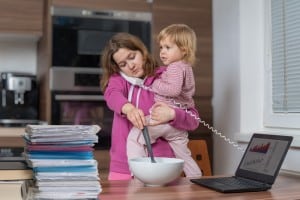 Mutter multitasking während Karenz mit Telefon, kochen & Kind