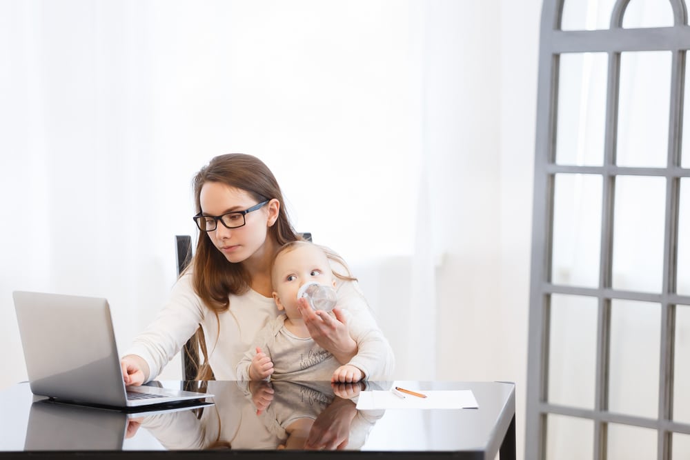 Mutter arbeitet während Karenz am PC mit Baby auf Schoß